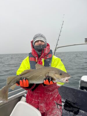 Boy holding arctic cod on a snowy day on sea