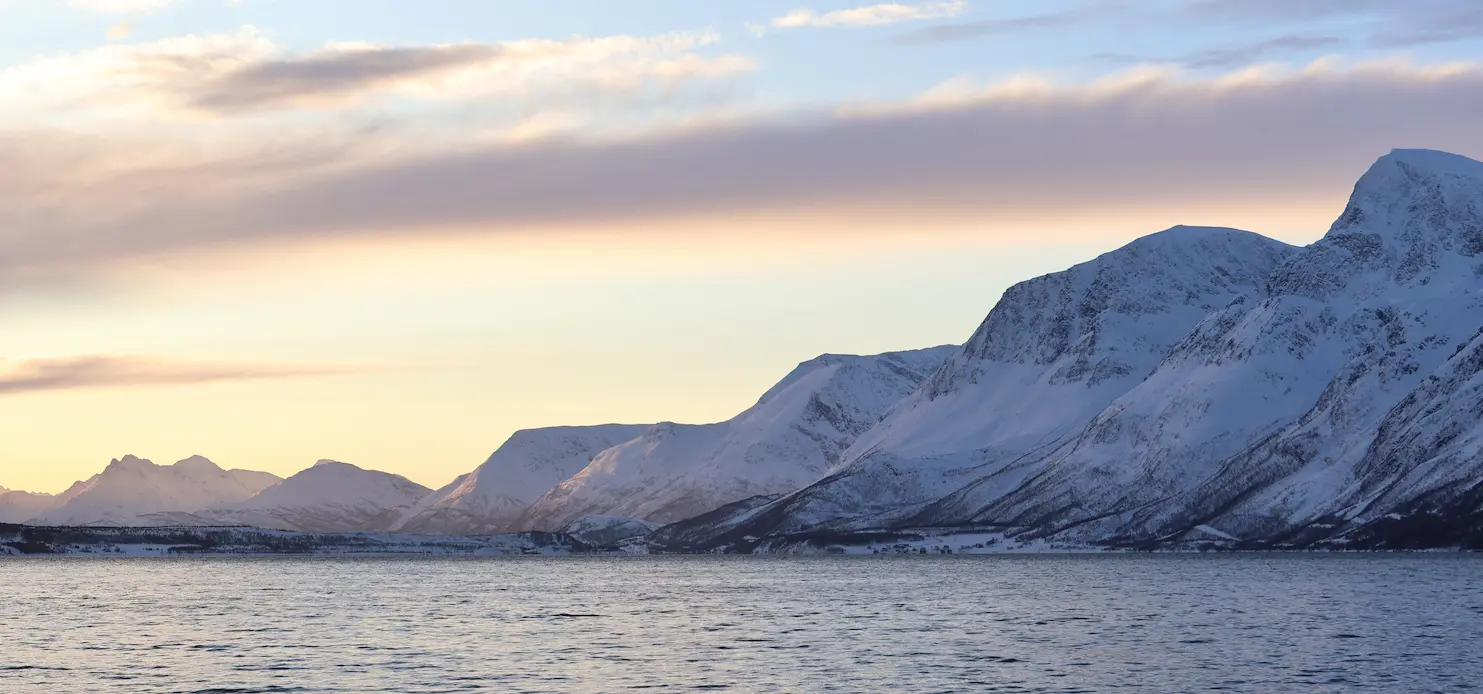 Golden winter sunset over Arctic fjord and snowy peaks near Tromsø