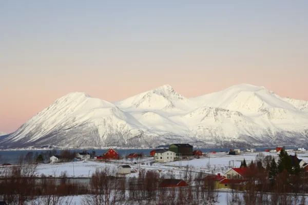 Small Arctic village with snow-covered houses and mountains in soft sunset light near Tromsø