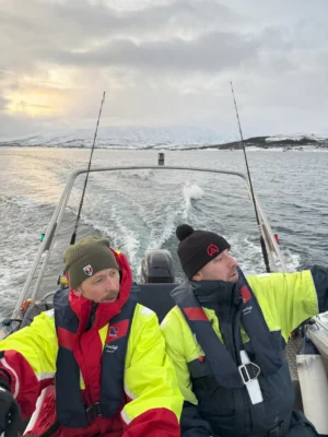 Two men in thermal suits navigating a fishing boat during a private Arctic tour near Tromsø
