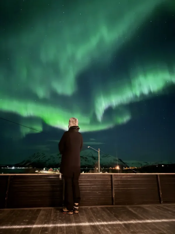 Girl enjoying a bright green Northern lights over a mountain near Tromsø