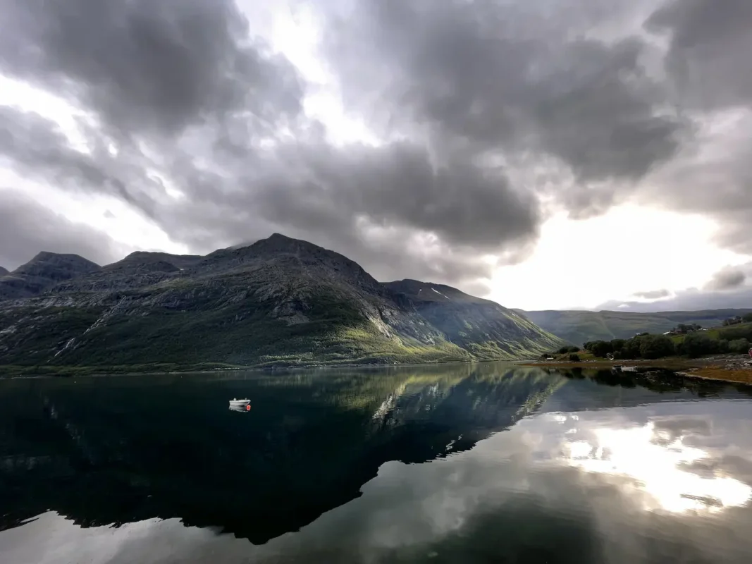 Cloudy skies over mountains and calm fjords an a small fishing boat near Lyngen