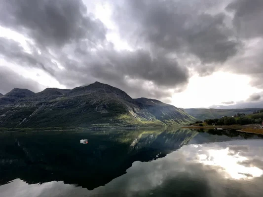 Cloudy skies over mountains and calm fjords an a small fishing boat near Lyngen