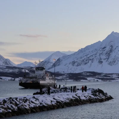 Ferry arriving at snowy pier with people watching in an Arctic fjord near Tromsø