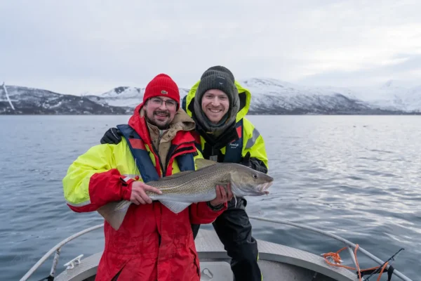 Two smiling guests holding a large cod on a private Arctic fishing boat tour near Tromsø in winter