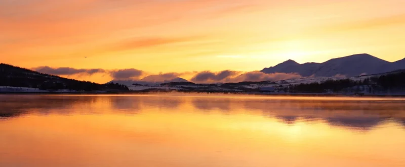 Golden winter sunset over Kvaløya with glowing sky reflected in calm Arctic fjord