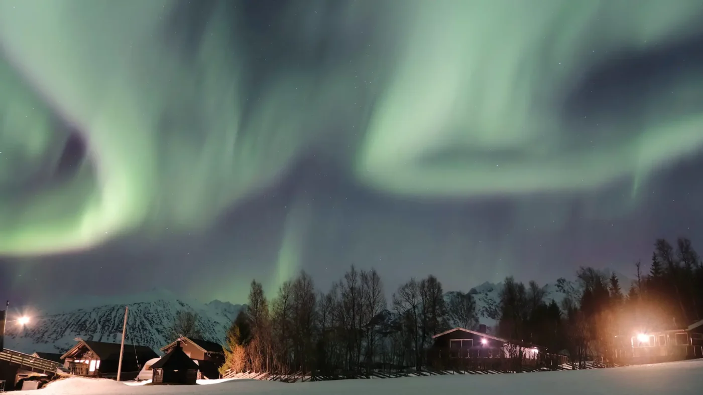 Northern lights dancing over mountain cabins near Lyngen Alps