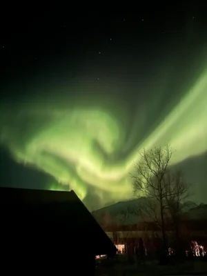 Whirlpool of Northern lights over a mountain and cabin near Lyngen