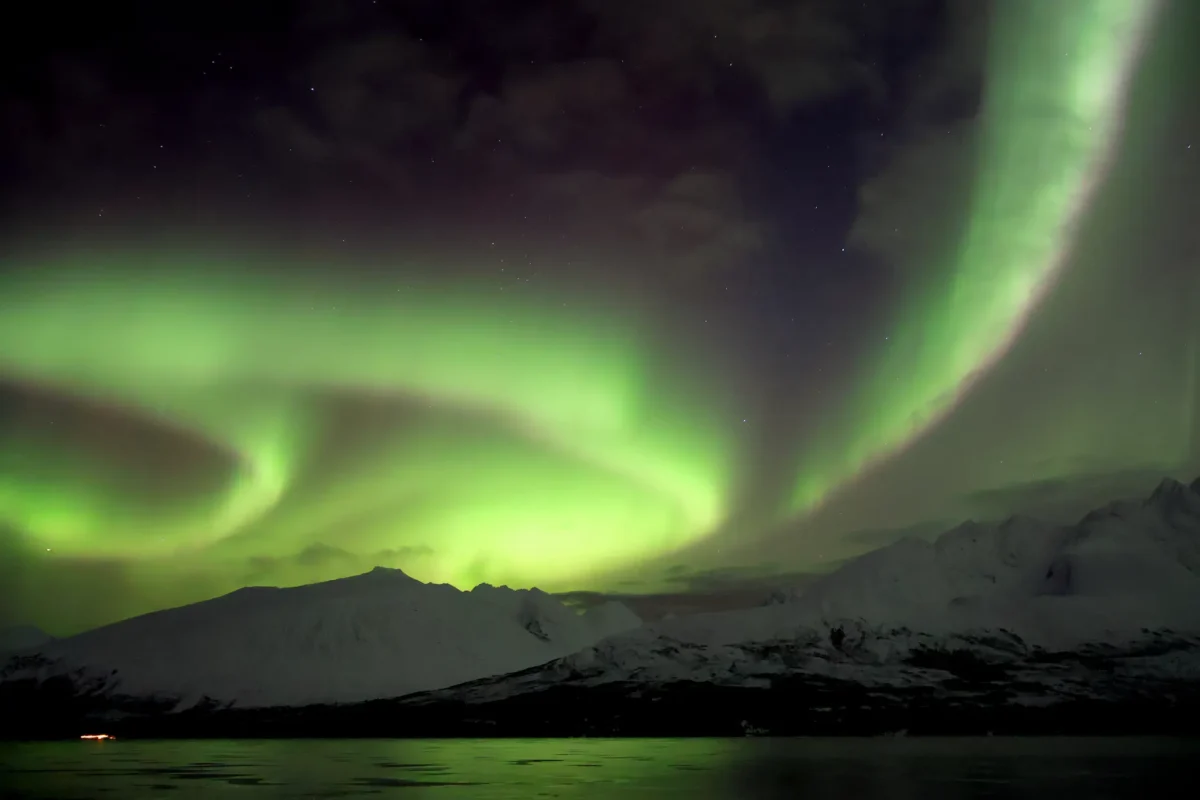 Bright spiral of Northern Lights glowing above snowy mountains and fjord near Tromsø