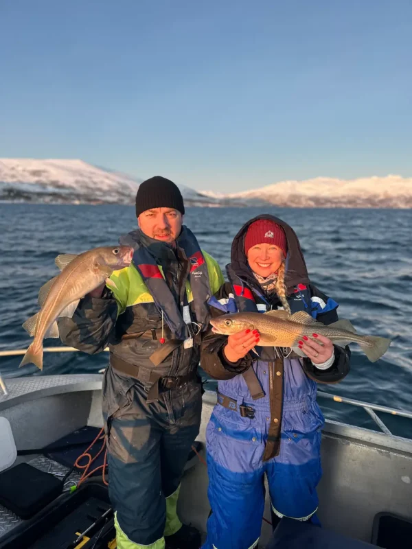 Happy couple holding a small fish caught on a fishing trip in Tromsø