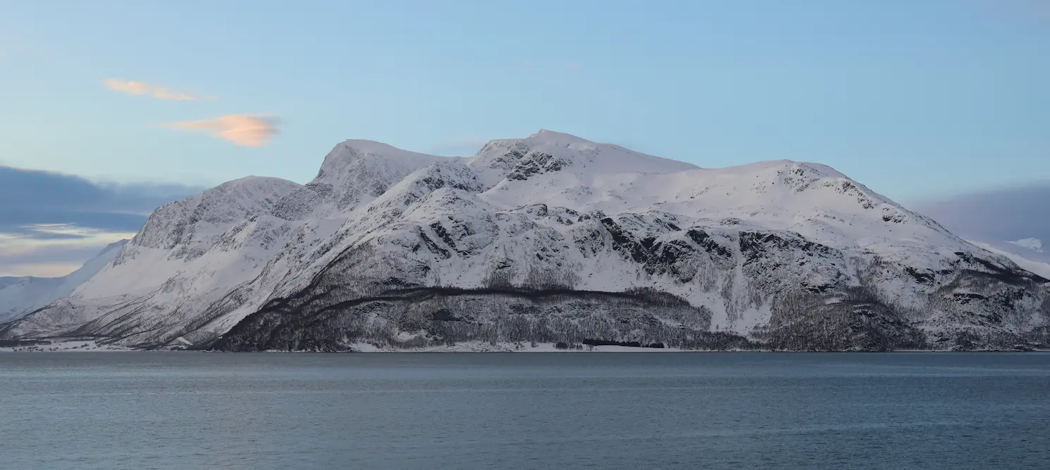 Snow-covered Arctic mountain rising above calm fjord near Tromsø, Norway