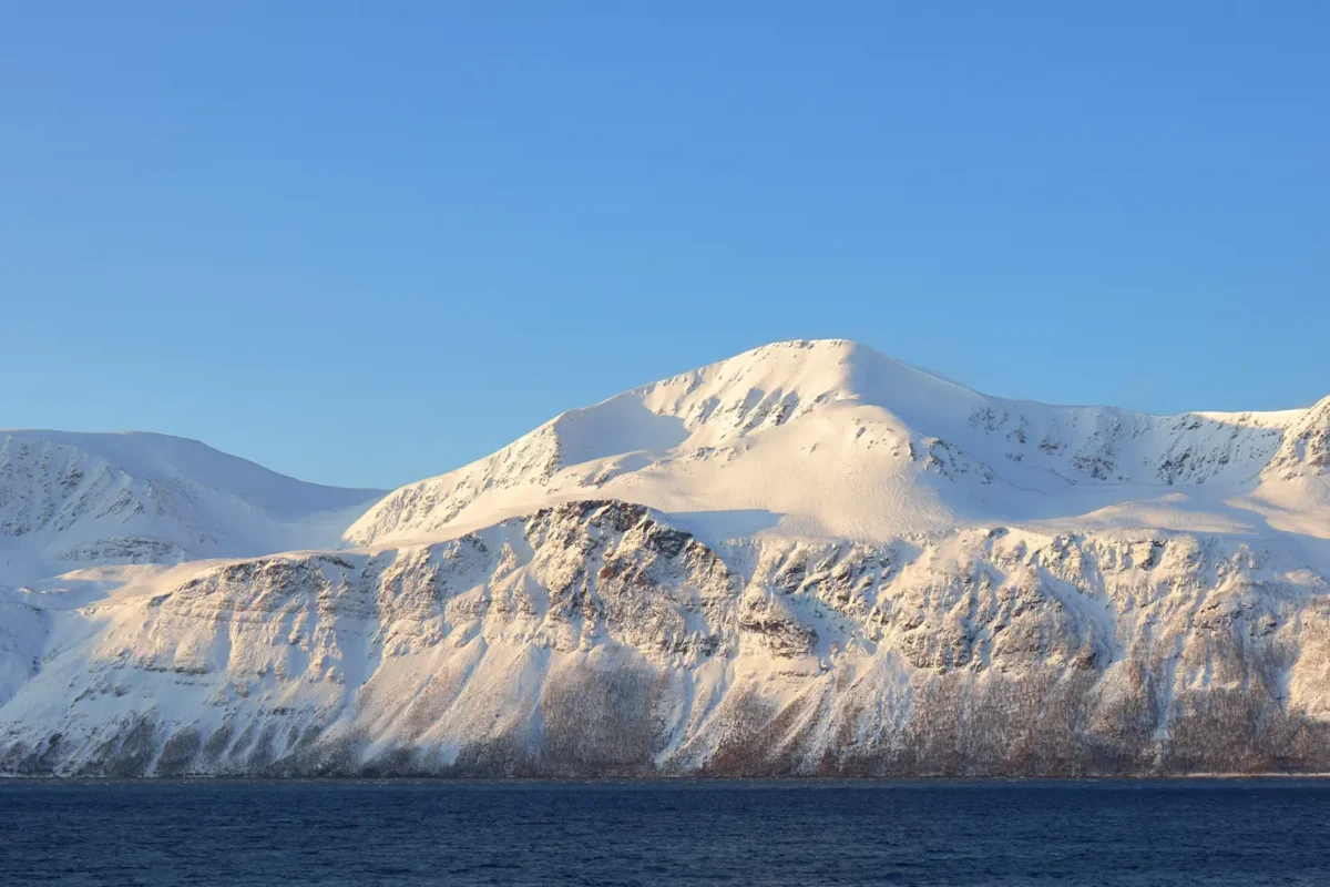 Sunlit Arctic mountain ridge above deep blue fjord in clear winter light near Tromsø