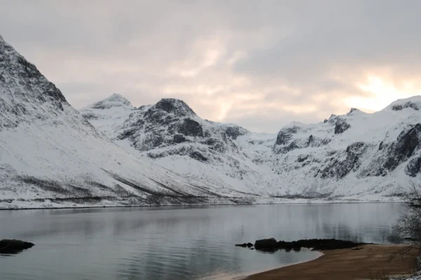 Snow-covered mountains reflecting in calm fjord waters near a sandy beach outside Tromsø