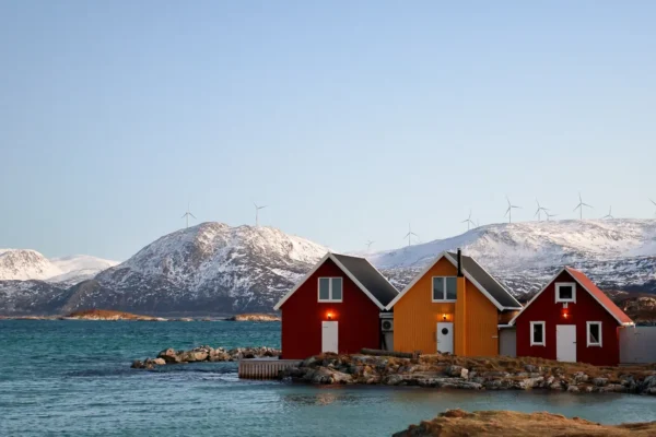 Most popular three colorful cabins by the fjord in Sommarøy with snowy hills and wind turbines in the background