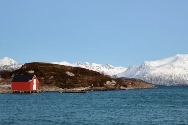 Red boat house by the fjord on Sommarøy island with snowy mountain peaks in the background