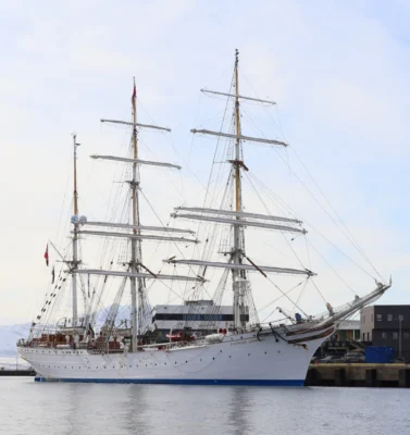 The tall ship Statsraad Lehmkuhl docked at Tromsø harbour with snowy peaks in the background