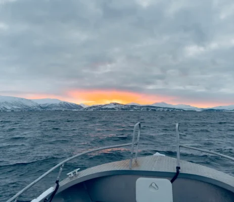 Fiery sunset over a snowy mountains viewed from a boat tour near Tromsø