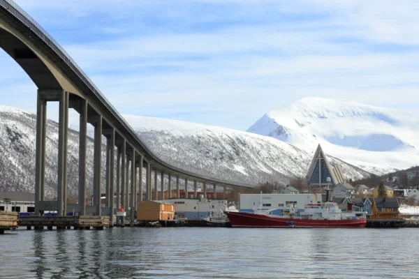 Tromsø Bridge stretching over the harbour with Arctic Cathedral and snowy mountain in the background