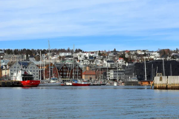 View of Tromsø city marina with sailboats, historic buildings, and snow-dusted houses on the hillside