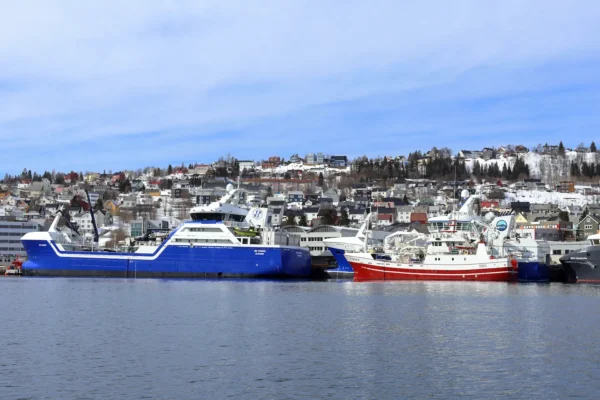 Fishing boats docked in Tromsø harbour with colorful hillside houses and snowy rooftops in the background