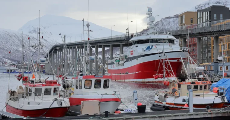 Fishing boats and large vessel docked in Tromsø harbour with Tromso bridge in background