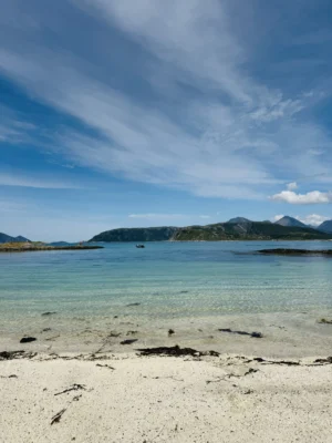 White-sand Arctic beach with clear turquoise water and mountains in the background near Sommarøy, Tromsø, Norway.