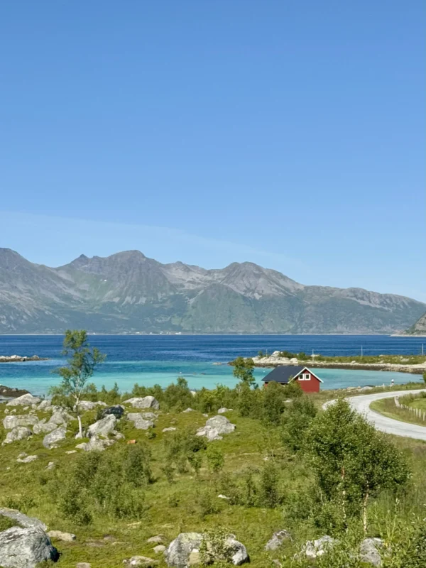 Red cabin overlooking turquoise fjord waters and mountains near Sommarøy, Tromsø, Norway.