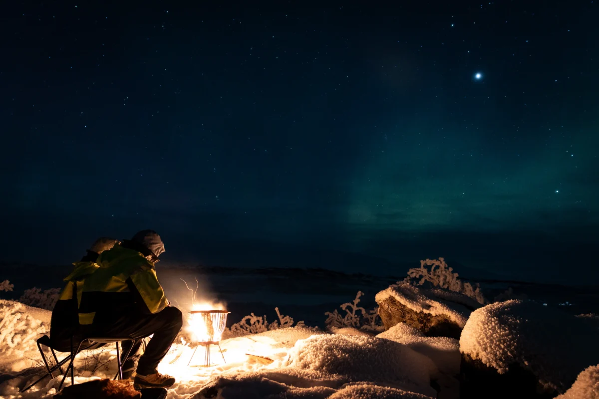 Guest warming by a campfire during a private Northern Lights tour in Tromsø
