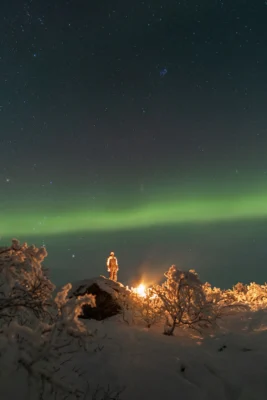Guest standing by a campfire under the Northern Lights during a private Northern Lights tour in Tromsø