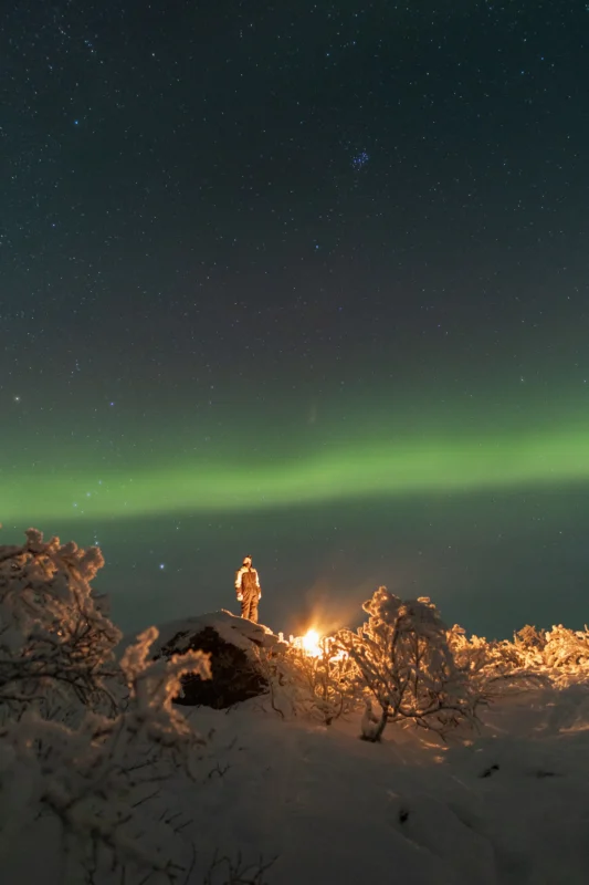Guest standing by a campfire under the Northern Lights during a private Northern Lights tour in Tromsø